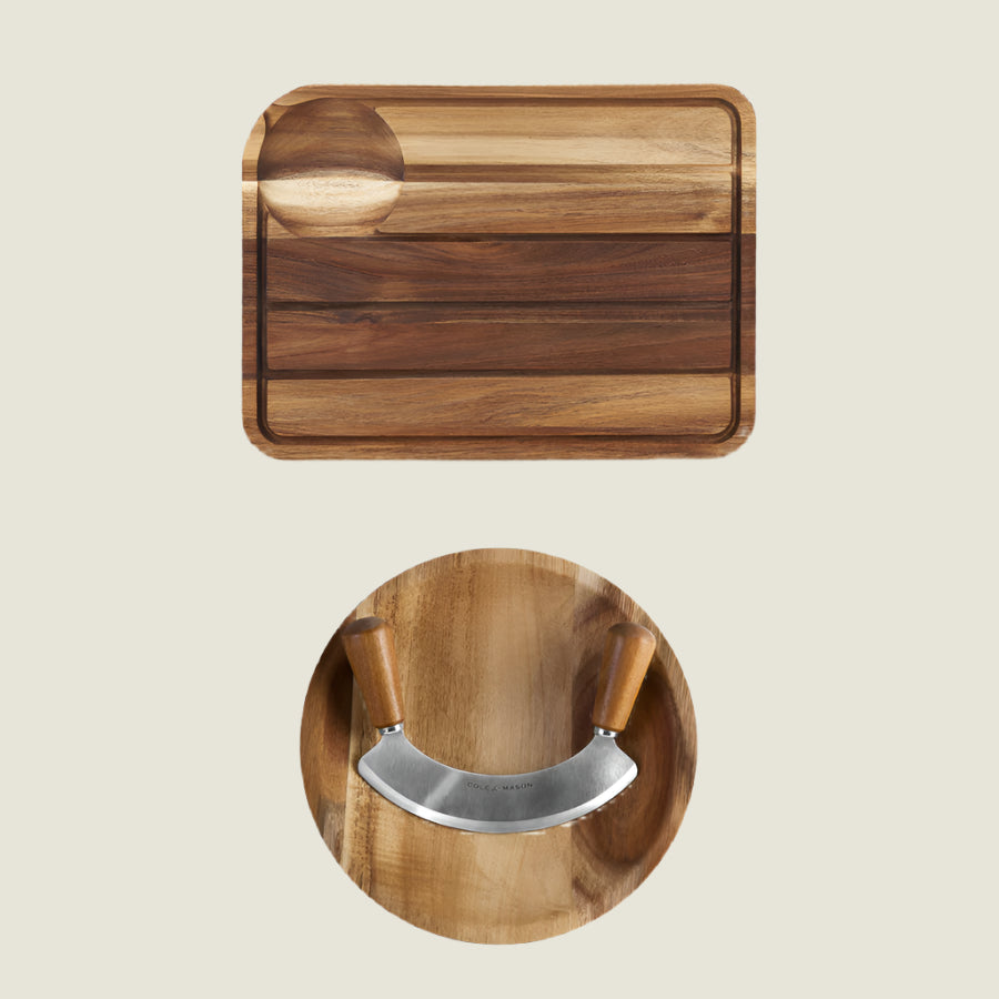 The Cole & Mason Berden Carving Board & Ashden Mezzaluna Bundle features a wooden board with a circular indentation and a crescent-shaped mezzaluna knife, both set atop an acacia wood bowl on a light background.
