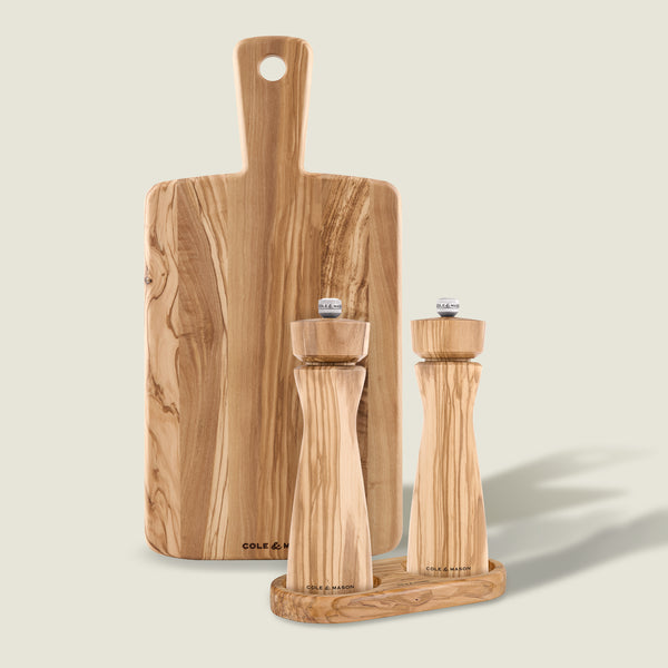 A Cole & Mason Portobello Mills, Tray & Small Serving Board set in light wood sits against a beige background, featuring matching Italian olive wood salt and pepper mills on a small tray with a serving board behind.