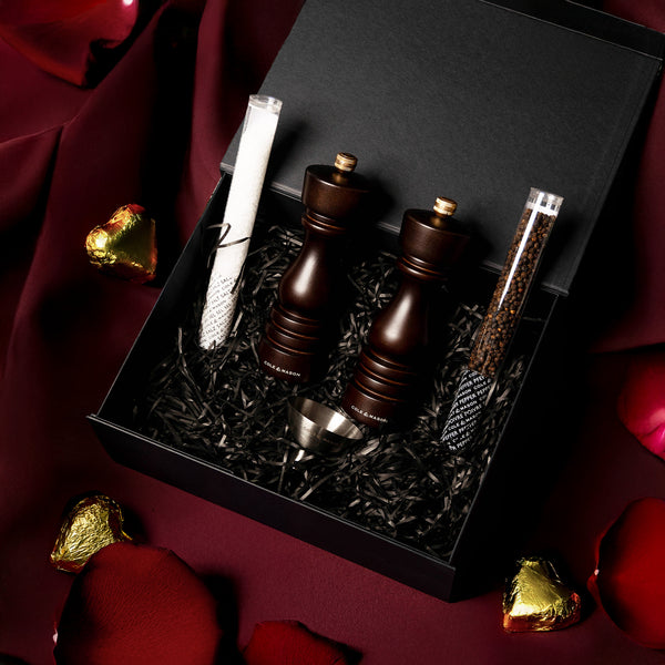The Cole & Mason London Chocolate Wood Mill Gift Hamper includes a Salt & Pepper Mill Set, metal funnel, salt and pepper tubes, and white cloth—perfect for gift hampers. Presented in a gift box with chocolates and rose petals.