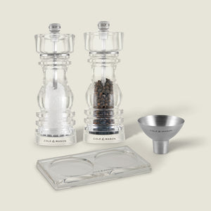 The Fast Bundle London Salt & Pepper Mill Set 180mm Bundle includes clear salt and pepper grinders, a small metal funnel, and a clear tray with two round indentations, all displayed on a plain background.