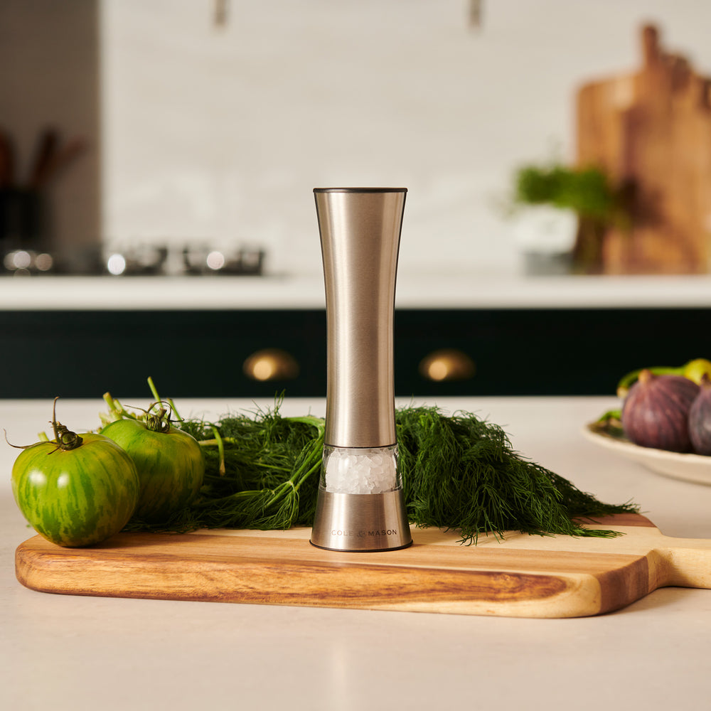 The Cole & Mason Burford Electronic Single Mill is a sleek stainless steel pepper grinder with adjustable grind settings, a transparent peppercorn chamber, and a labeled base. It casts a soft shadow against a light background.