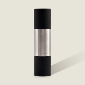 The Cole & Mason Clevedon 2-in-1 Mill features a modern cylindrical design with black matte ends and a brushed stainless steel center, standing upright on a light beige background—an innovative grinder ideal for contemporary kitchens.