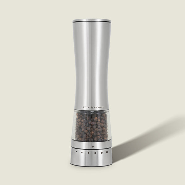 A sleek, silver Cole & Mason Electric Derwent Pepper Mill with a transparent lower section displaying black peppercorns stands upright on a light background.