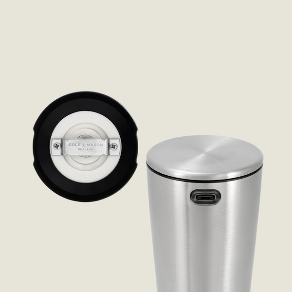 The image shows a stainless steel cylindrical Electric Derwent Salt & Pepper Mill with a USB-C charging port; next to it is a close-up of a round white and black component featuring the Cole & Mason brand, likely the base or interior of the lid.
