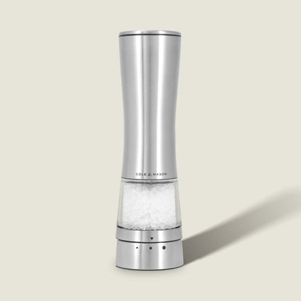 A Cole & Mason Electric Derwent Salt & Pepper Mill, crafted from stainless steel with a transparent base filled with coarse salt, stands upright on a light beige background.
