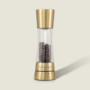 The Cole & Mason Derwent Gold Salt & Pepper Mill features gold-tone stainless steel, advanced grinding technology, and is filled with black peppercorns, all set against a plain, light background.