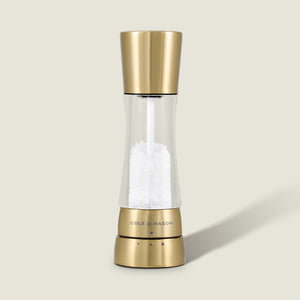 The Cole & Mason Derwent Gold Salt Mill, a gold-tone stainless steel grinder filled with coarse salt, stands upright on a neutral background, showcasing sleek modern style and advanced grinding technology.