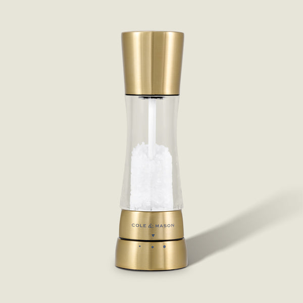 The Cole & Mason Derwent Gold Salt Mill, a gold-tone stainless steel grinder filled with coarse salt, stands upright on a neutral background, showcasing sleek modern style and advanced grinding technology.