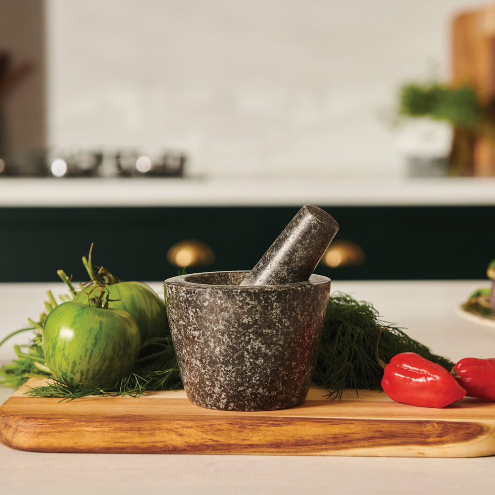 The Cole & Mason Dorchester Granite Pestle & Mortar, in dark gray with speckled detail, sits on a light background. The pestle rests inside the bowl, angled right—ideal for grinding herbs or making fresh spice blends.