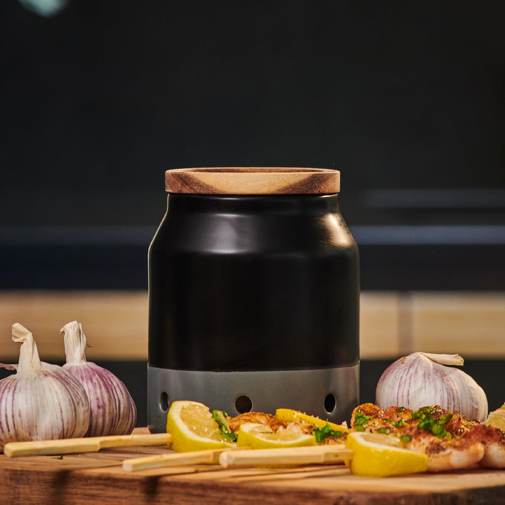 The Cole & Mason Elmdon Ceramic Garlic Keeper, in black and gray with a wooden lid and round ventilation holes, offers stylish garlic storage and appears against a light background.