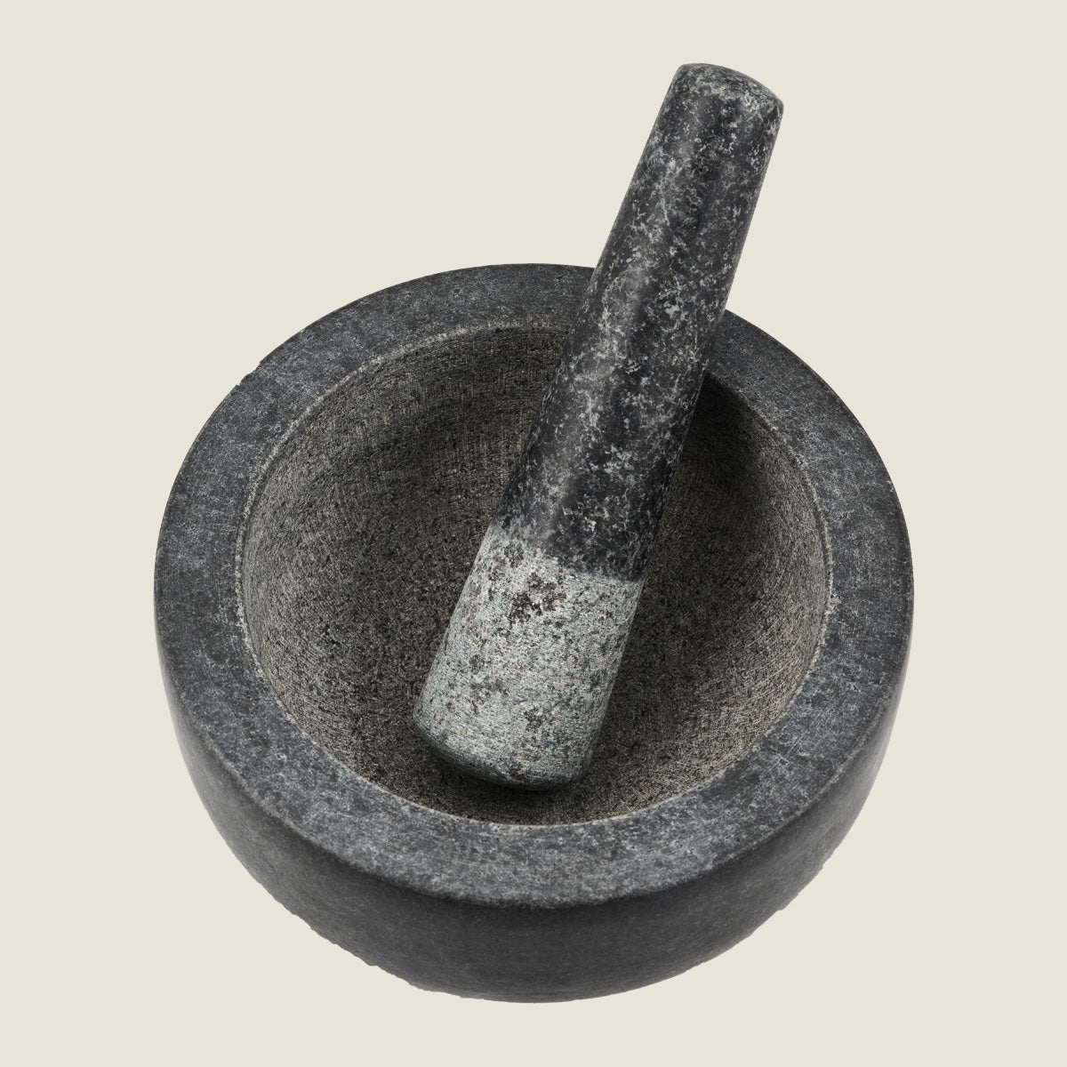 A dark gray stone mortar and pestle set, with the pestle resting inside the bowl, photographed from above on a light background.