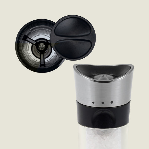 A close-up of Cole & Mason’s Horsham Salt & Pepper Mills shows a stainless steel top, black accents, and visible salt crystals, with the open lid from above revealing its high-performance grinding mechanism.