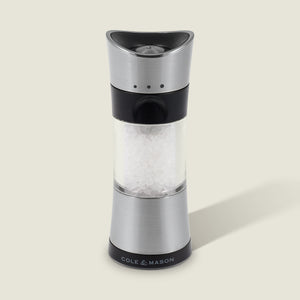A Cole & Mason Horsham Salt & Pepper Mill in stainless steel and clear acrylic, filled with coarse salt, stands upright on a light background with a right-side shadow and the COLE & MASON logo at its base.