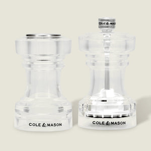 A pair of Cole & Mason Acrylic Salt Shaker & Pepper Mill Set (104 mm) are displayed side by side on a light background. Both mills feature clear acrylic bodies with the Cole & Mason logo at the base, flat and round tops, and visible grinding mechanisms that allow you to adjust the coarseness of your spices for a customizable seasoning experience.