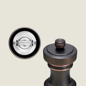 A close-up of the Cole & Mason Hoxton Salt and Pepper Mill, featuring antique bronze and copper accents, highlights the grinding system and the “P” label on top.