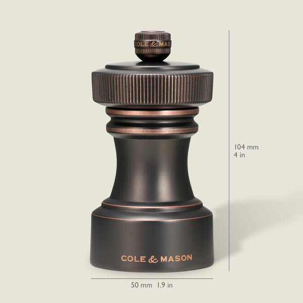 A dark metallic pepper grinder from the Cole & Mason Hoxton Salt and Pepper Mill Set in an antique bronze finish is shown upright against a light background, labeled with the brand name. The mill measures 104 mm (4 in) tall and 50 mm (1.9 in) wide, and features a precise grinding system for consistent seasoning—perfect for pairing with any salt or pepper mill set.
