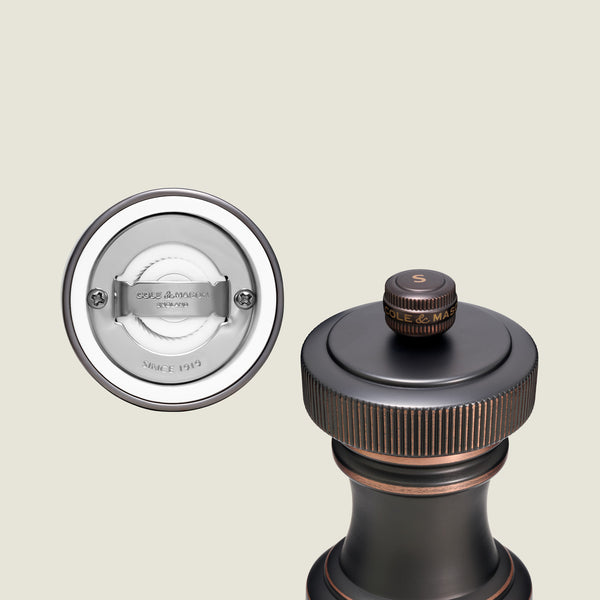 A close-up of the Cole & Mason Hoxton Salt and Pepper Mill Set in antique bronze, featuring a gold “S” on top, elegantly displayed alongside a view of its silver grinding mechanism.
