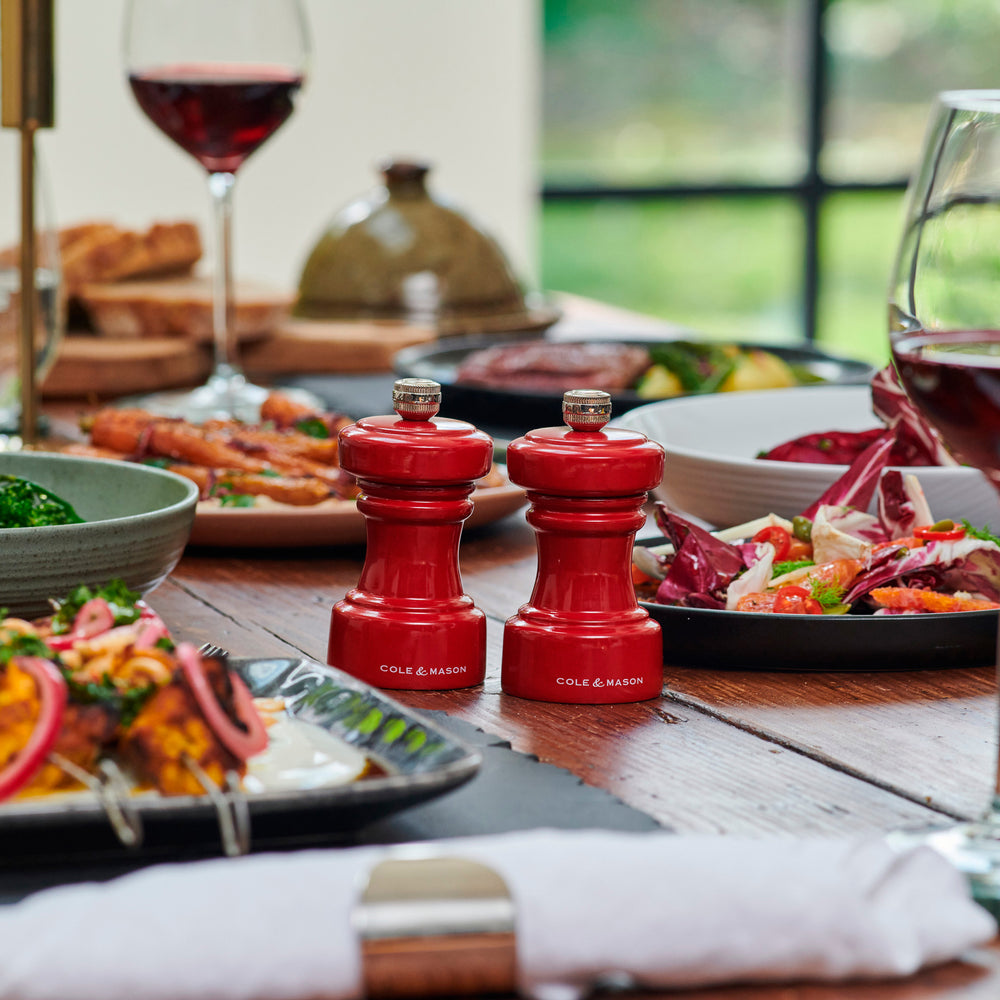 The Cole & Mason Hoxton Red Gloss Mill Christmas Gift Hamper includes two red mills, three spice tubes, and a metal funnel in black shredded paper—ideal for Christmas hamper boxes.