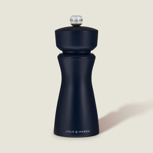 A Persian Blue Cole & Mason Kenton Salt & Pepper Mill, featuring a high-quality ceramic grinder and a sleek design, stands upright on a light beige background, casting a soft shadow to the right.