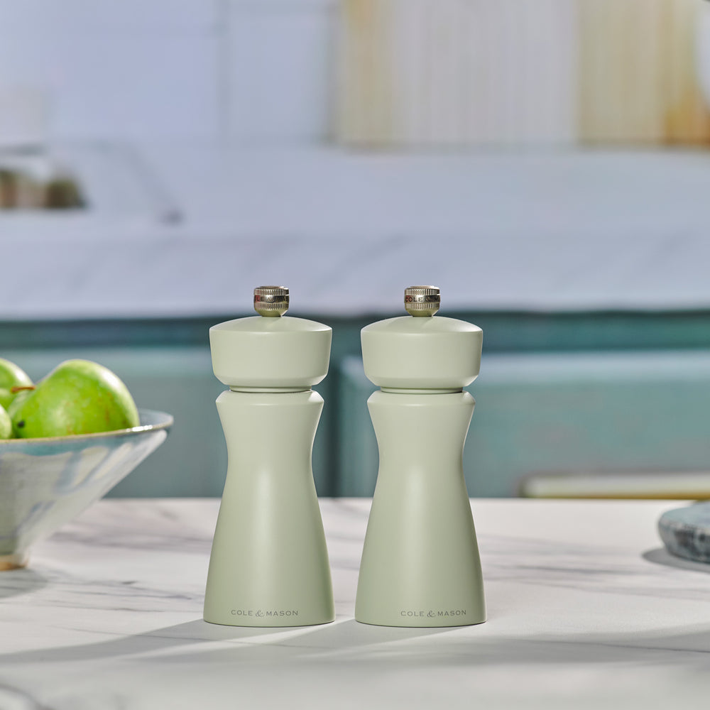 The Cole & Mason Kenton Sage Salt & Pepper Mill features a light green finish, a silver top knob, and a durable ceramic mechanism. It stands upright against a plain, off-white background.