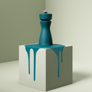 A teal Cole & Mason Mix & Match Kenton Mills dual-use grinder stands on a light gray cube with teal paint dripping down its sides, set against a minimalist background in soft, neutral tones.