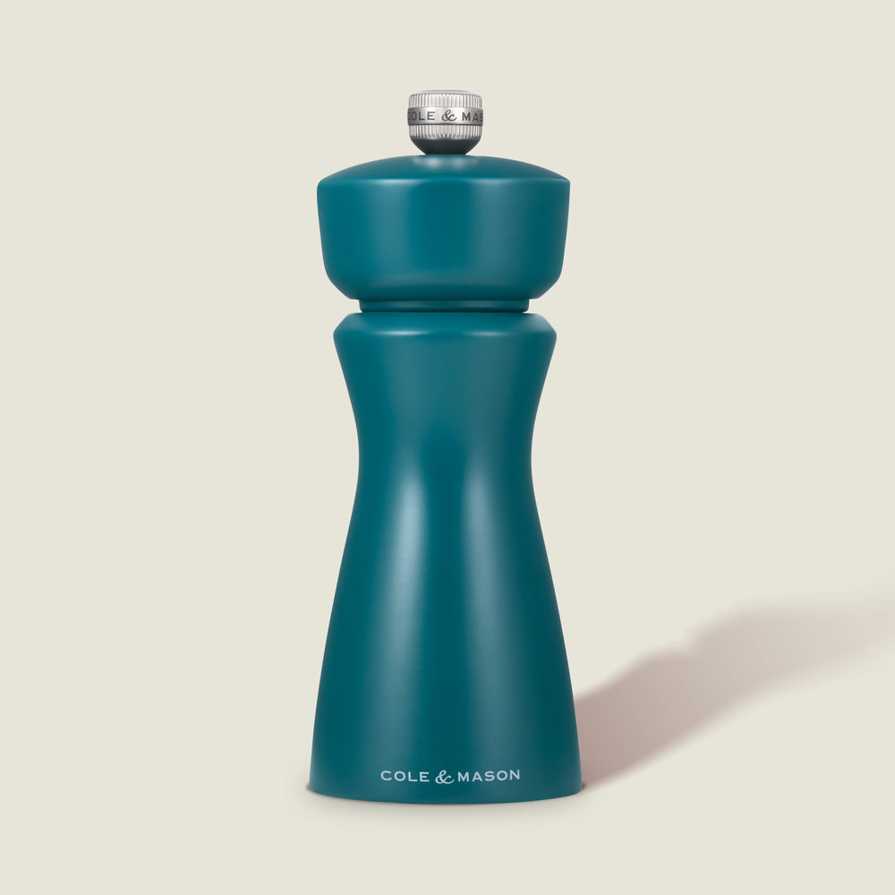 The Cole & Mason Kenton Sea Salt Blue Salt & Pepper Mill, with a ceramic mechanism and sleek curved design topped by a silver knob, stands upright against a light beige background—ideal for modern kitchens.