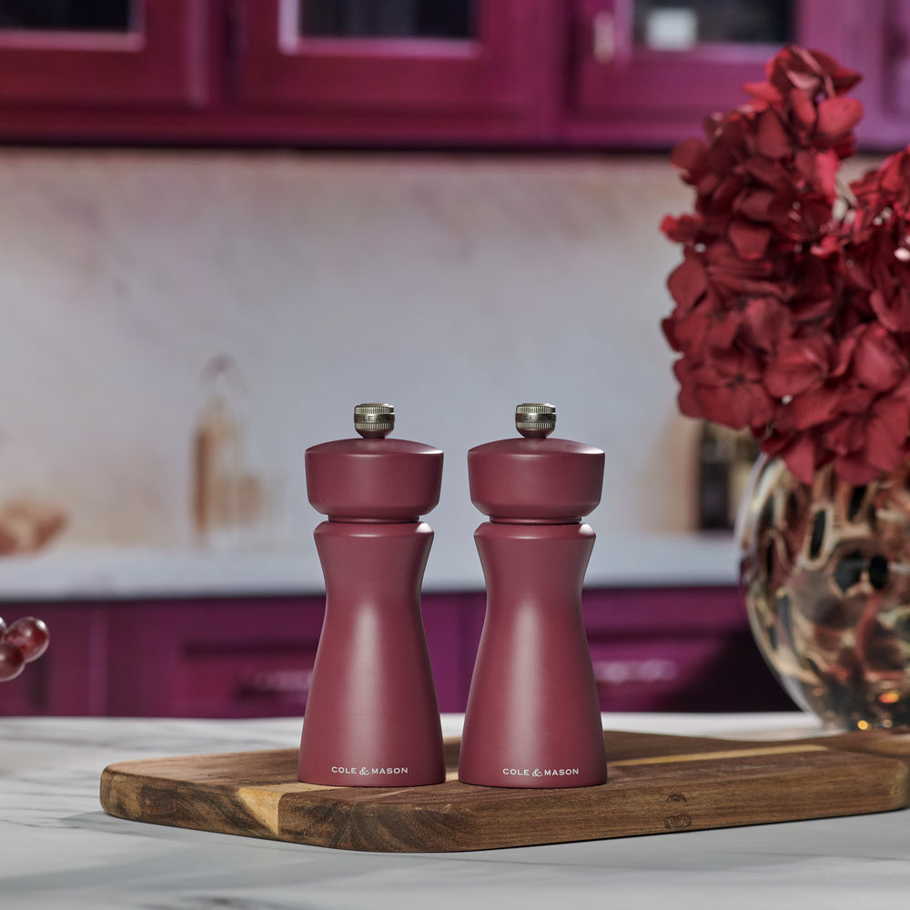 The Cole & Mason Kenton Sichuan Pepper Red Salt & Pepper Mill, with a matte burgundy finish, ceramic mechanism, and silver top knob, stands upright on a plain light background with the brand logo in white near its base.