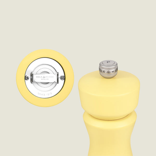The Cole & Mason Kenton Salt & Pepper Mill in Turmeric is displayed with a close-up of its ceramic grinding mechanism and branded base. A silver knob labeled "P" is featured on top.