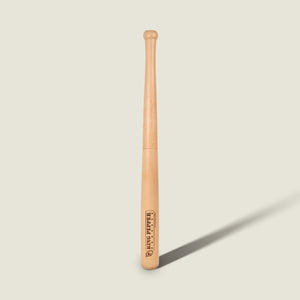 A light wooden baseball bat stands upright against a plain, light background, casting a shadow to the right. Much like the Cole & Mason King Pepper Baseball Bat Pepper Mill 710mm—with its engraved logo and text near the thick end—this bat showcases careful craftsmanship and subtle detailing.