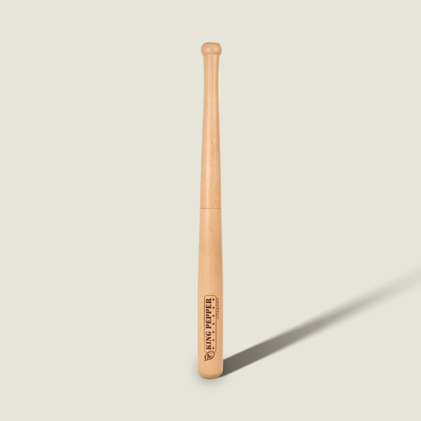 A light wooden baseball bat stands upright against a plain, light background, casting a shadow to the right. Much like the Cole & Mason King Pepper Baseball Bat Pepper Mill 710mm—with its engraved logo and text near the thick end—this bat showcases careful craftsmanship and subtle detailing.