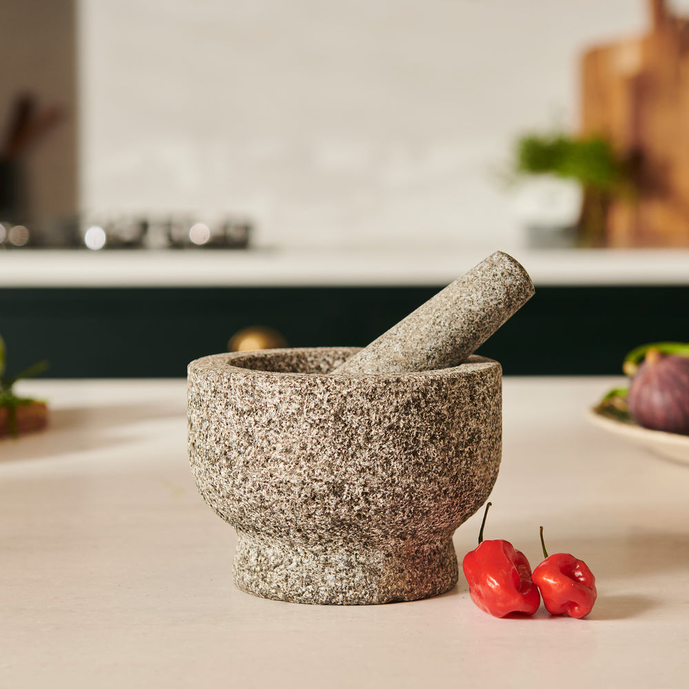 The Cole & Mason Langley Pestle & Mortar, made from natural granite in gray, features the pestle resting inside the mortar and is displayed on a light neutral background—perfect for preparing spice rubs.