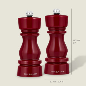 A pair of Cole & Mason London Red Acrylic Salt & Pepper Mills, each measuring 150 mm (6 in) tall and 57 mm (2.24 in) wide, stand side by side. With a glossy red finish, adjustable grinding mechanisms, and sleek metal tops, they are set against a neutral light beige background.