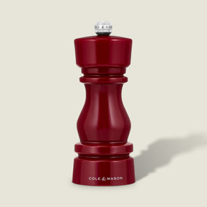 A glossy red pepper grinder from Cole & Mason's London Red Acrylic Salt & Pepper Mills 150mm collection stands upright on a light beige background, featuring a silver knob, the Cole & Mason logo at its base, and an adjustable ceramic grinding mechanism.