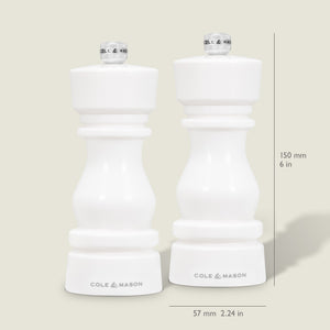 Two Cole & Mason London White Acrylic Salt & Pepper Mills (150mm) stand side by side on a light background. Each features an adjustable grinding mechanism and measures 57mm wide, with measurement lines shown beside the contemporary design.