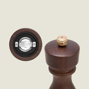 A close-up of the Cole & Mason London Walnut Salt or Pepper Mill highlights the grinding mechanism on the bottom and a top view with a brass knob labeled “P.”.