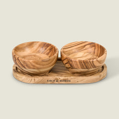 The Cole & Mason Portobello Olive Wood Pinch Pot Set features two small pinch pots with natural grain on a matching oval tray, engraved with COLE & MASON, against a plain light beige background.