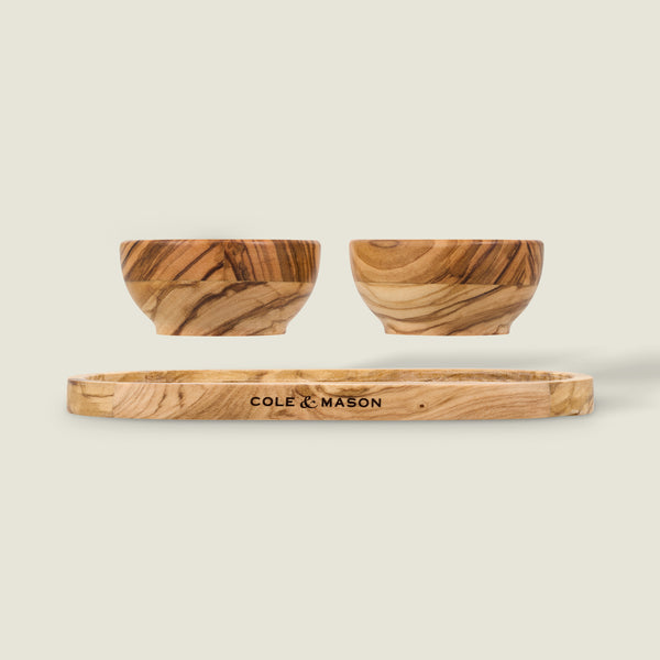 The Cole & Mason Portobello Olive Wood Pinch Pot Set includes two small olive wood pinch pots and a matching seasoning tray, all engraved with the brand name and set against a plain, light background.