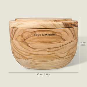 The Cole & Mason Portobello Olive Wood Salt Cellar is a round salt holder with lid, featuring a natural wavy grain. Measuring 90mm wide by 64mm tall, it displays the brand on the front and adds rustic Italian style to your kitchen.