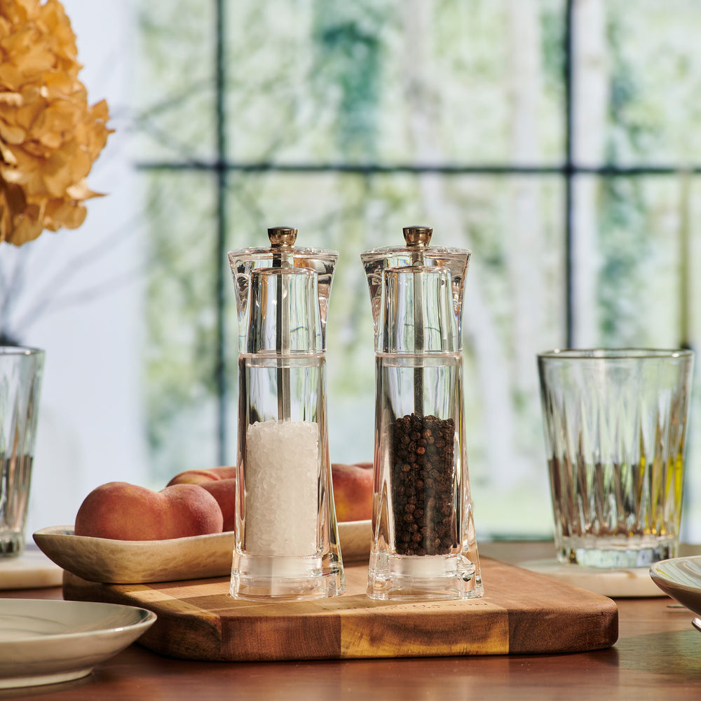 The Cole & Mason UK Prism Salt & Pepper Mill Set Acrylic 165mm features two clear mills—one with white salt crystals, the other with black peppercorns—each with adjustable grind and durable stainless steel mechanism, set side by side on a plain background.