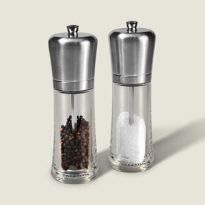 The Cole & Mason Sandown Salt & Pepper Mill Set features clear glass mills with stainless steel tops, filled with black peppercorns and coarse salt, and offers adjustable grinding for perfect seasoning control.