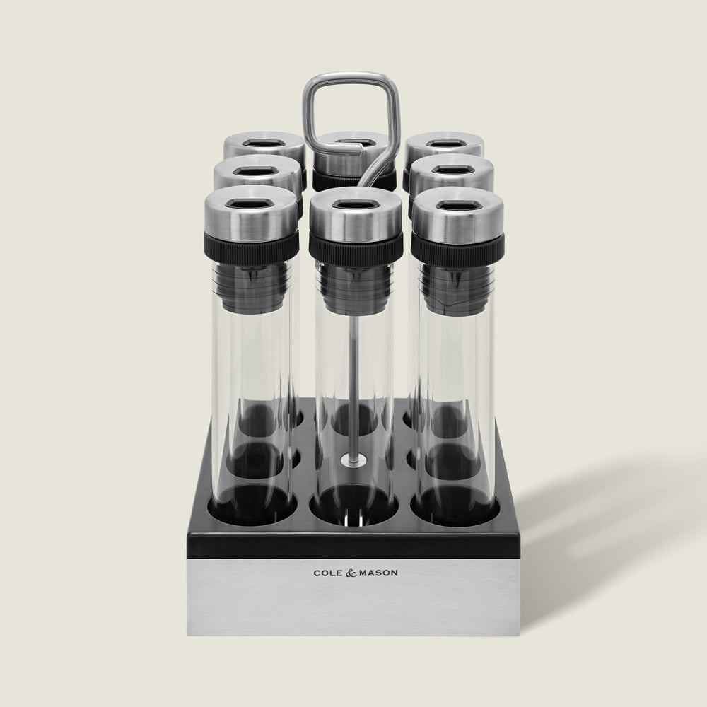 The Cole & Mason Shadwell Countertop Spice Storage features eight airtight glass jars in a stainless steel square holder with a metal handle for easy countertop organization.