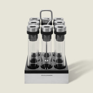 The Cole & Mason Shadwell Countertop Spice Storage features eight airtight glass jars in a stainless steel square holder with a metal handle for easy countertop organization.