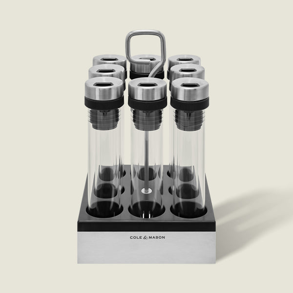 The Cole & Mason Shadwell Countertop Spice Storage features eight airtight glass jars in a stainless steel square holder with a metal handle for easy countertop organization.
