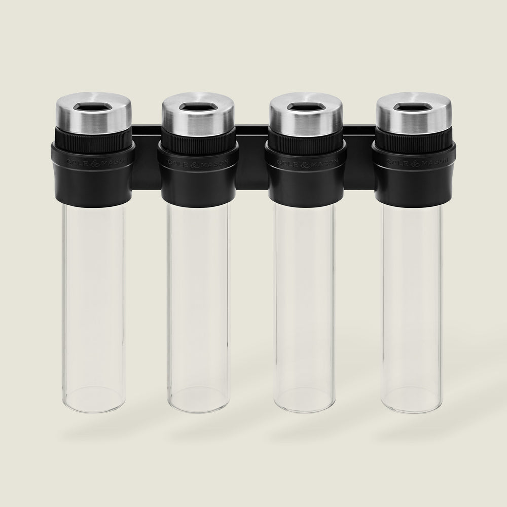 The Cole & Mason Shadwell Slim-Mount Spice Storage features four clear airtight glass containers with silver lids in a vertical black wall rack—ideal for stylish herb and spice storage.