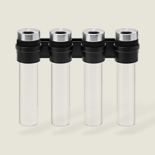 The Cole & Mason Shadwell Slim-Mount Spice Storage features four clear airtight glass containers with silver lids in a vertical black wall rack—ideal for stylish herb and spice storage.