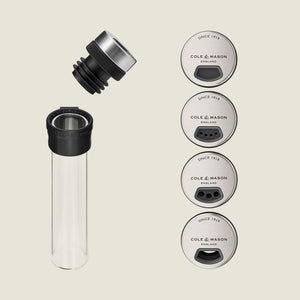The Shadwell Countertop Spice Storage by Cole & Mason features a transparent grinder with black and metal cap, plus four labeled metal lids offering different grind sizes—perfect for spice rack or countertop use.