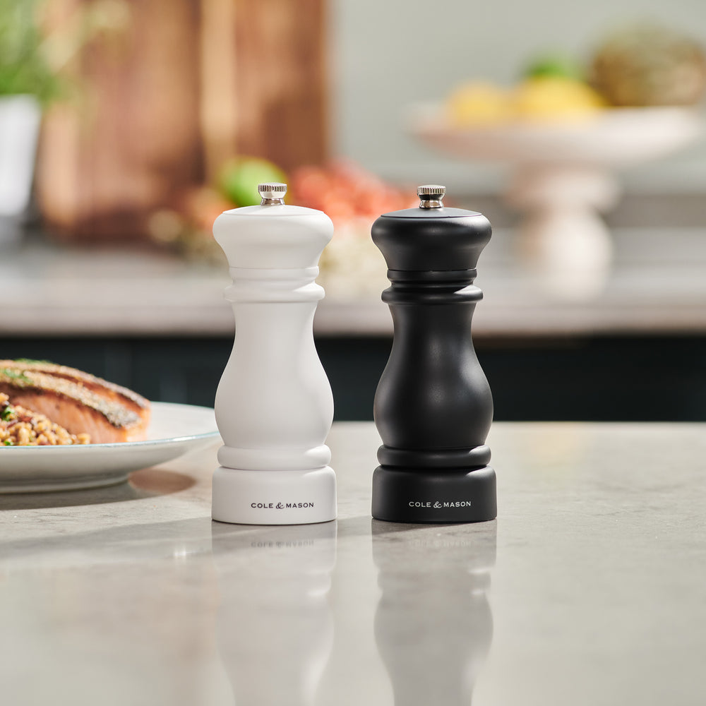A white and black Cole & Mason Southwold Capstan Salt & Pepper Mill set, featuring a classic hourglass shape and sturdy build, are displayed side by side on a light background.