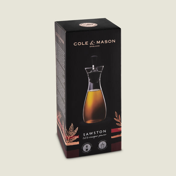 The Cole & Mason Sawston Oil & Vinegar Pourer comes in a sleek black box with gold accents, showcasing the ergonomic pourer filled with liquid on the front and product info on the sides for controlled pouring.