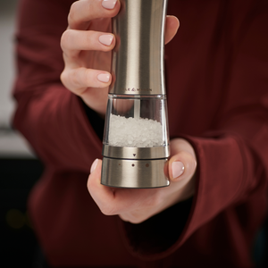 A person wearing a maroon sleeve holds a Cole & Mason Electric Derwent Salt & Pepper Mill filled with coarse salt, ready to season food.