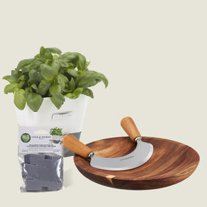 The Cole & Mason Single Herb Keeper, Chopper & Refills Bundle includes a white-potted basil plant, soil pod packet, wooden bowl, and stainless steel Mezzaluna chopper—everything you need to prepare fresh herbs with ease.